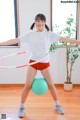 A woman in a white shirt and red shorts holding a hula hoop.