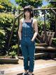 A woman in overalls standing on a wooden deck.