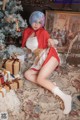 A woman in a red and white dress sitting on a rug next to a Christmas tree.